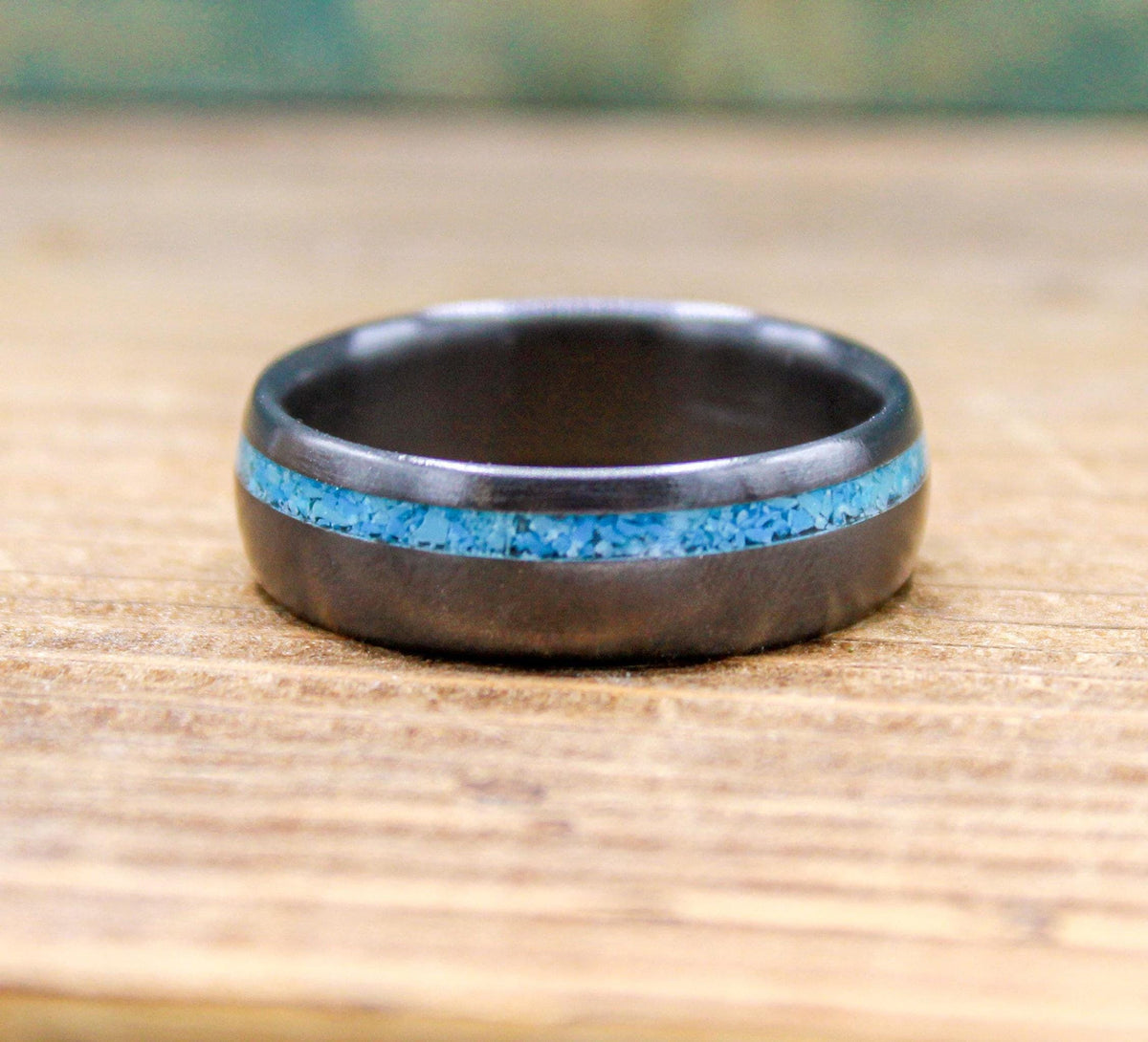 A dark ring with a blue inlay rests alone on a wooden surface.