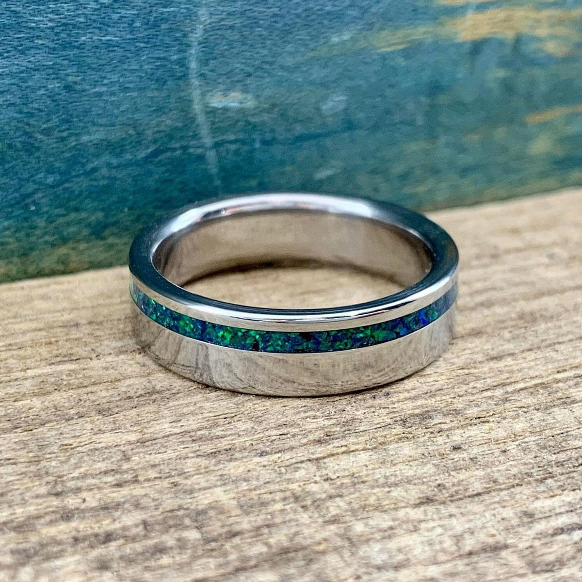 A straight-on view of a metallic ring showcasing its continuous green and blue speckled opal inlay.