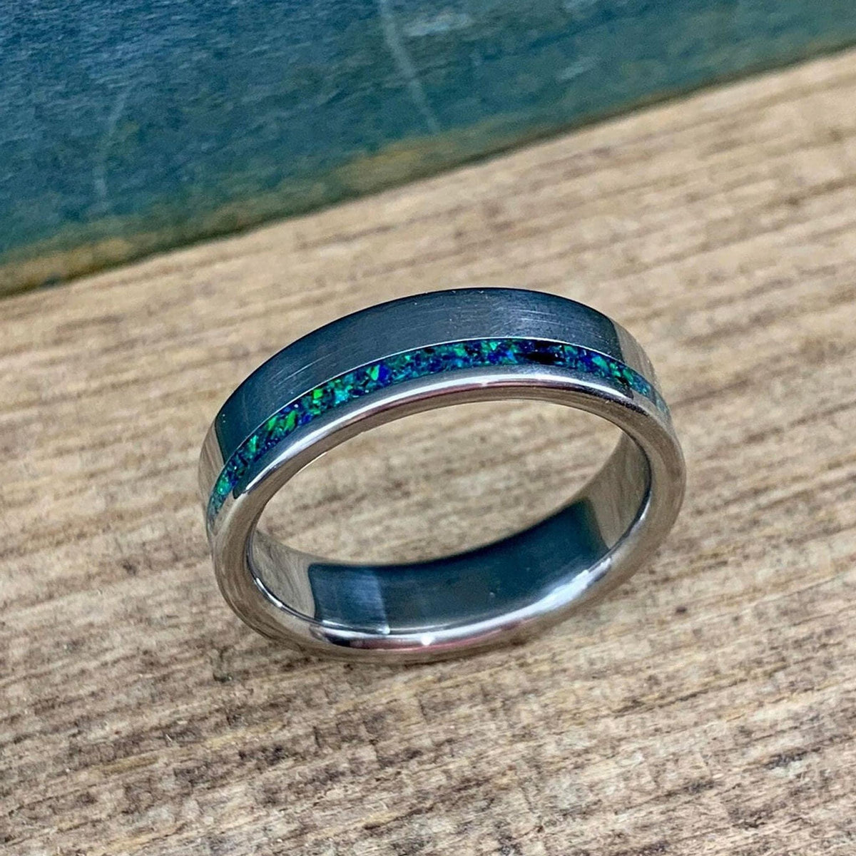A brushed-finish ring featuring a sparkling green and blue opal band running around its circumference.