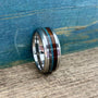 A metal ring featuring inlays of wood, meteorite, and turquoise resting on a wooden surface against a blue backdrop.