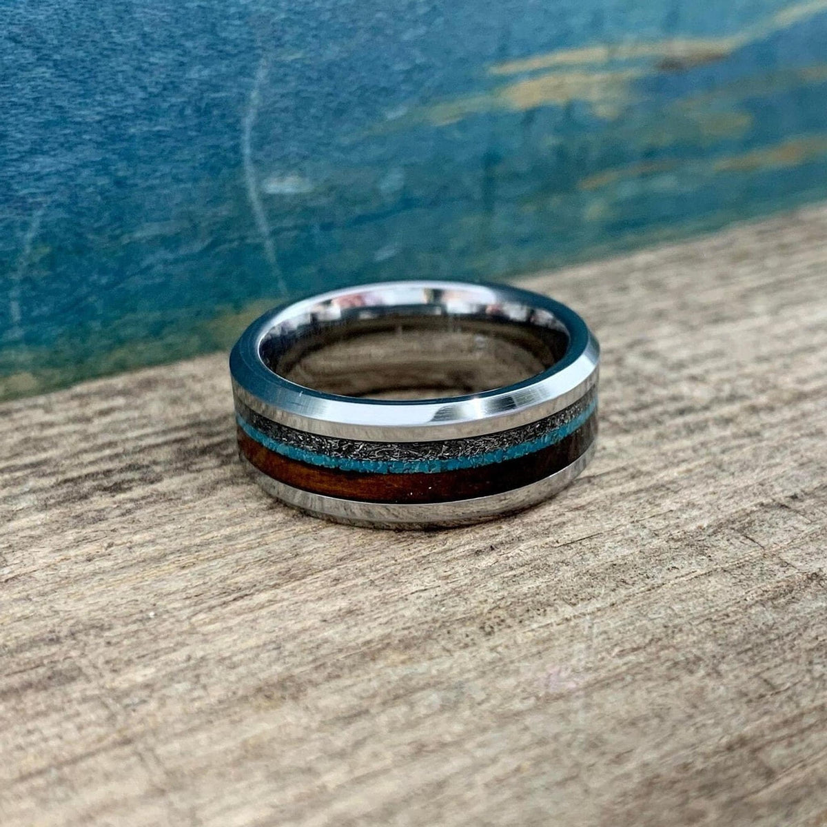 A ring with wood and turquoise inlays positioned horizontally on a weathered wooden background.