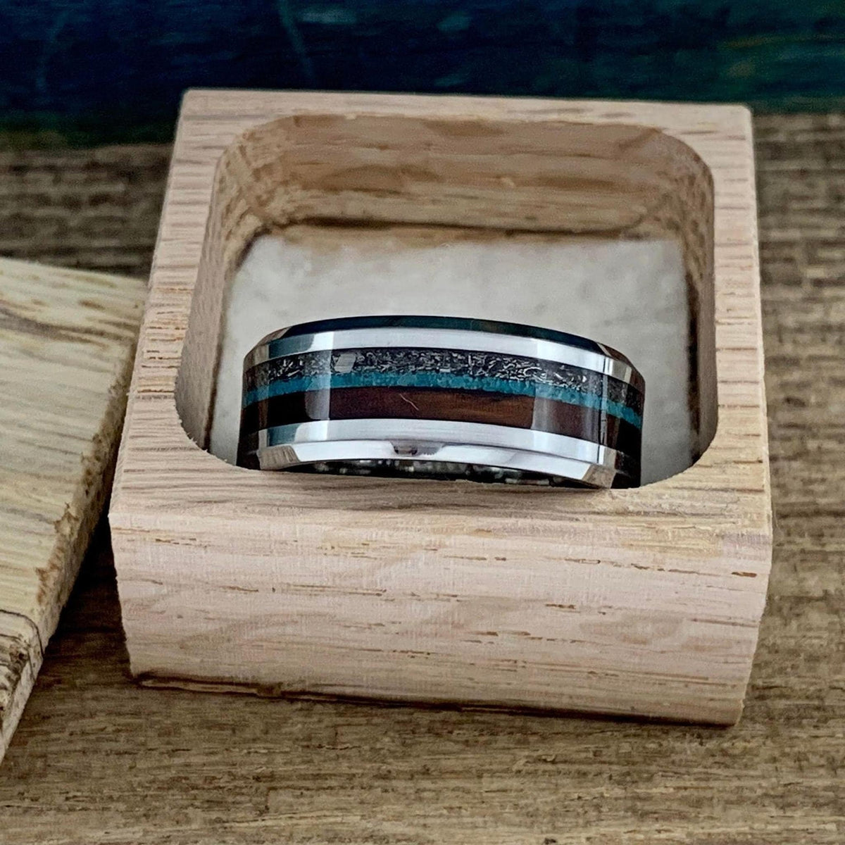 A banded ring placed upright inside a small wooden gift box with a white cushion.