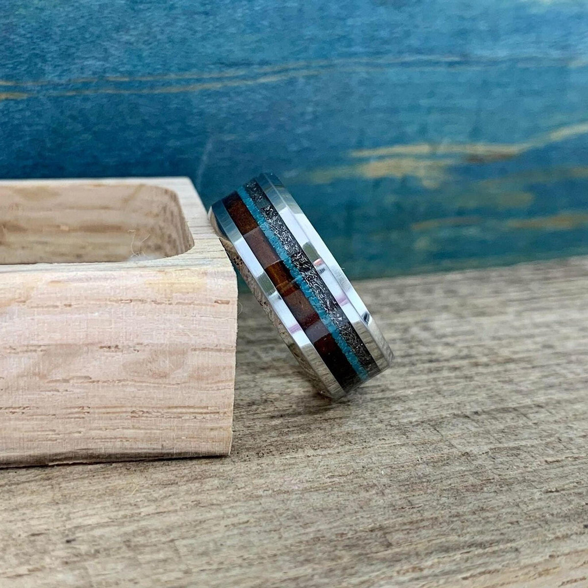 A ring with multiple inlays standing next to a small wooden block on a wooden surface.