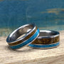 Two metal rings featuring turquoise and tiger's eye inlays, positioned side by side on a weathered wooden surface.