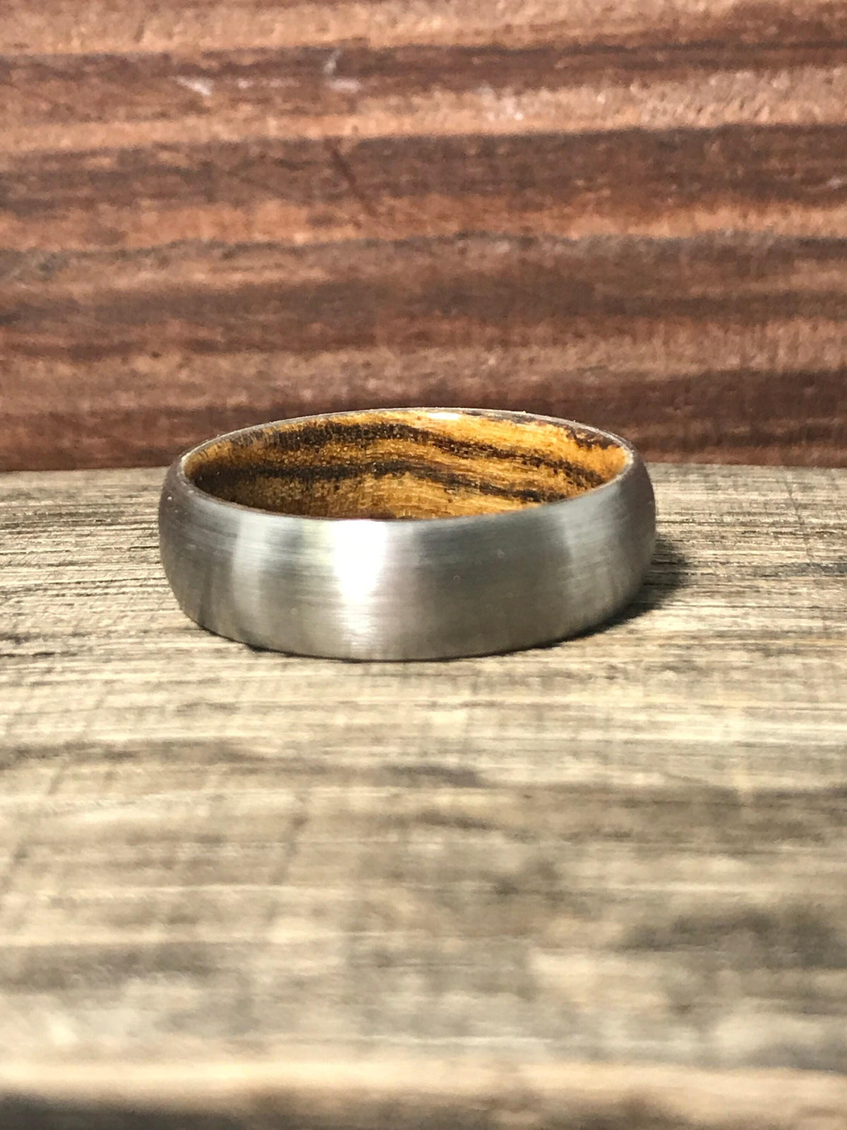 A brushed metal band ring with a wooden interior lies flat on a wooden surface.