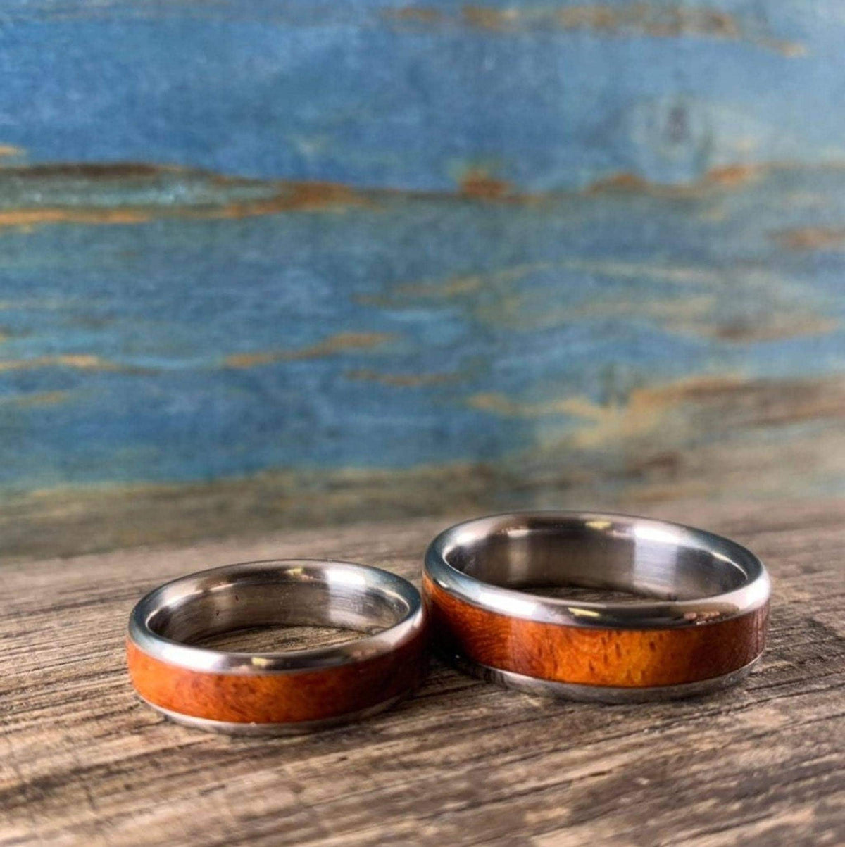 Two metal rings with distinctive wood inlays are positioned on a wooden plank in front of a blue wall.