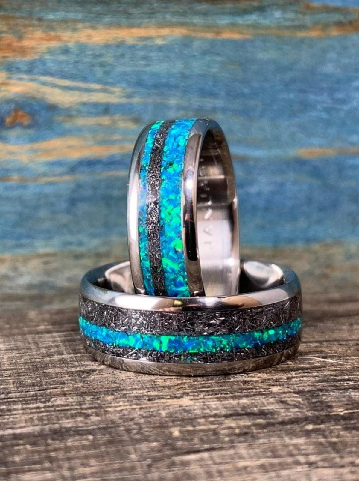 Two titanium wedding bands with meteorite and blue-green opal inlays, featuring one ring standing vertically inside the other.
