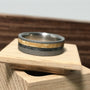 A sandblasted titanium wedding band featuring wood and meteorite inlays rests on a small wooden block.