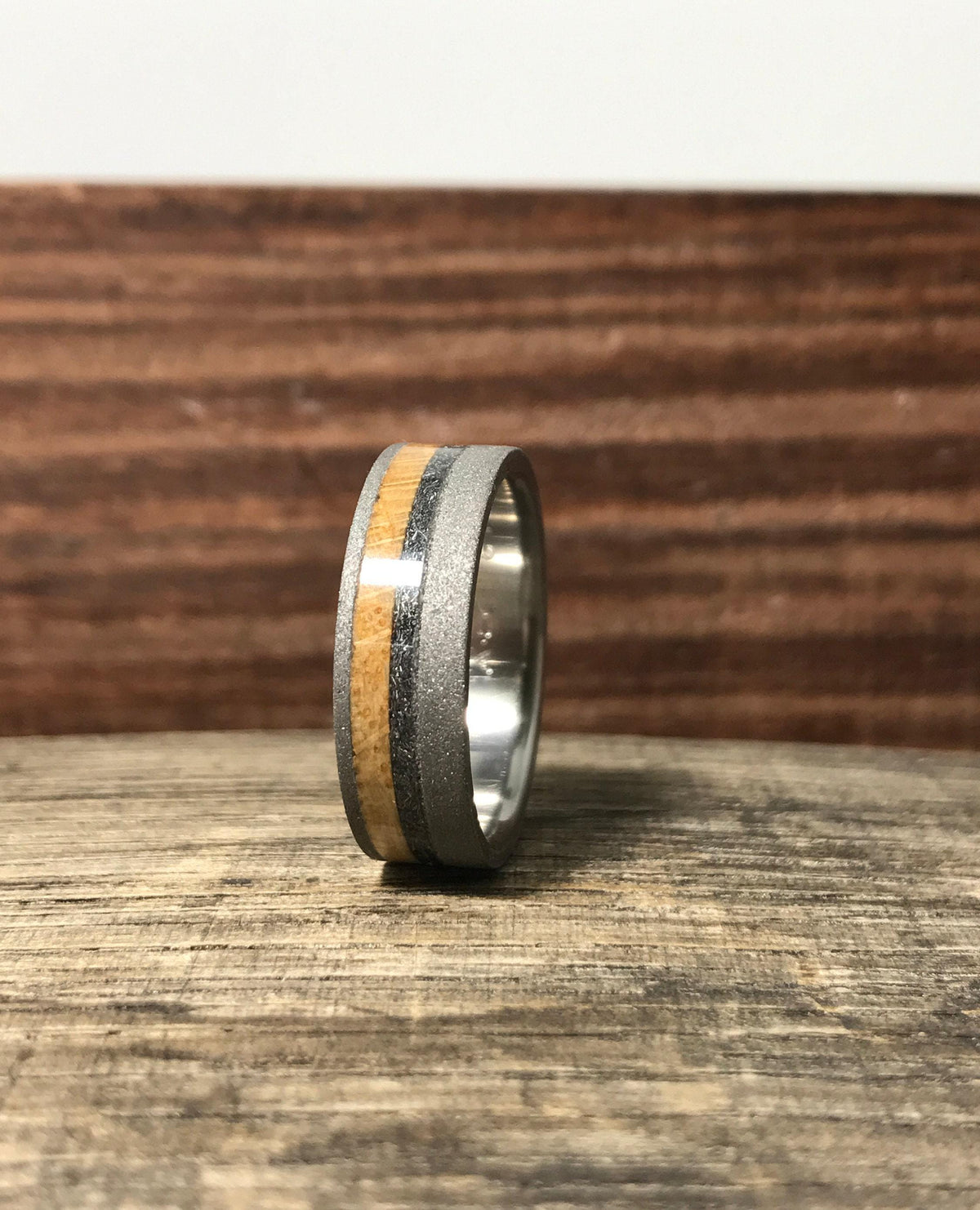 A side view of the titanium wedding band showing the sandblasted exterior and inlaid wood and meteorite stripes.