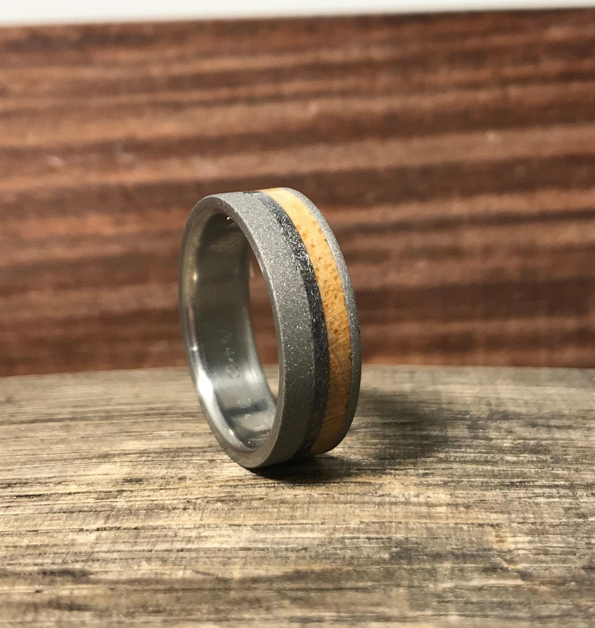 The titanium ring rests on its edge, showcasing the polished interior and the distinct wood and meteorite exterior bands.