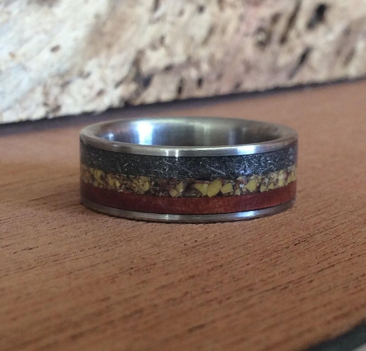 A close-up view of the multi-material ring resting flat on a wooden tabletop with a rustic wooden background.