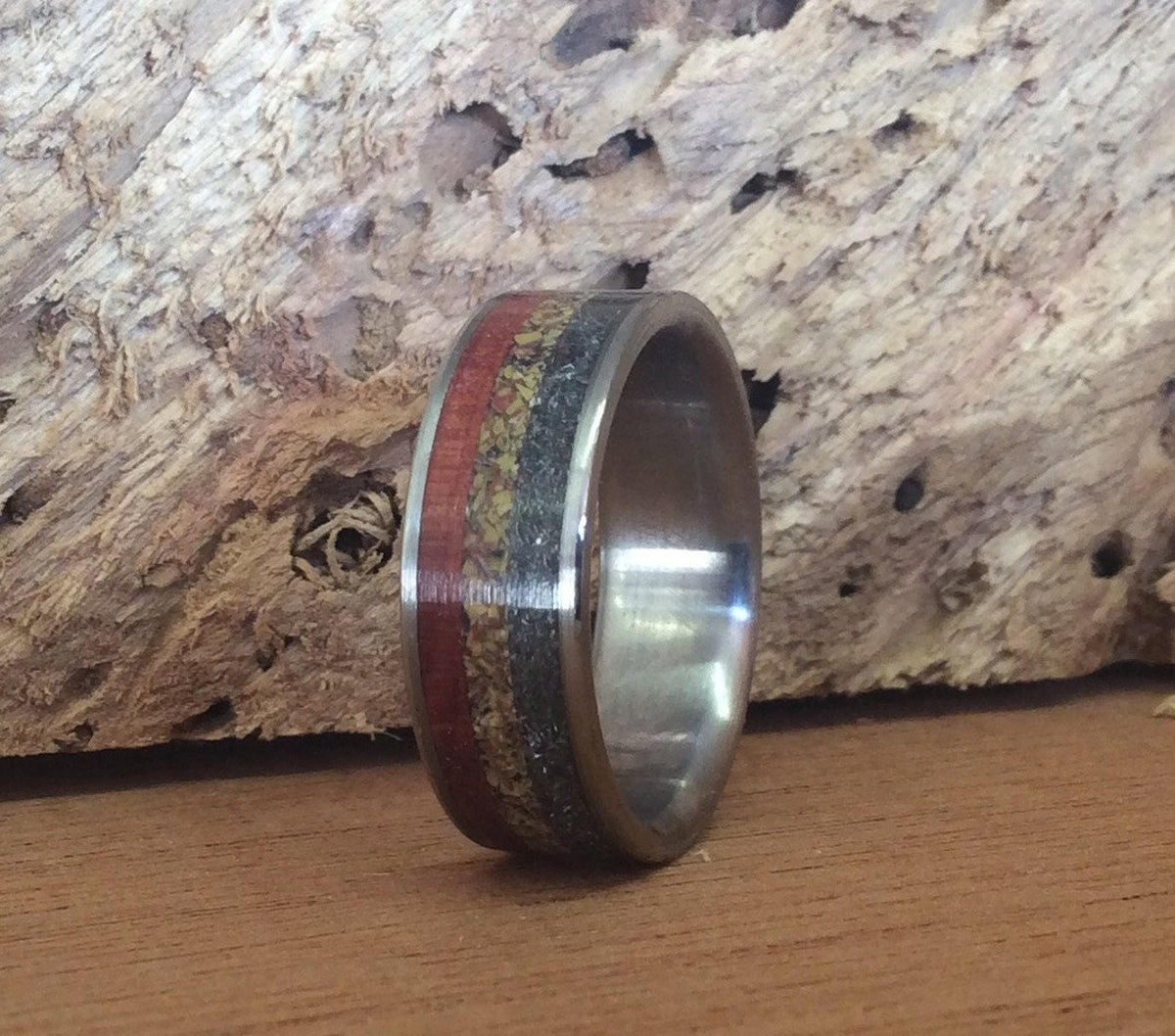 The ring angled slightly, displaying its polished interior and distinct wood, fossil, and meteorite inlay pattern.