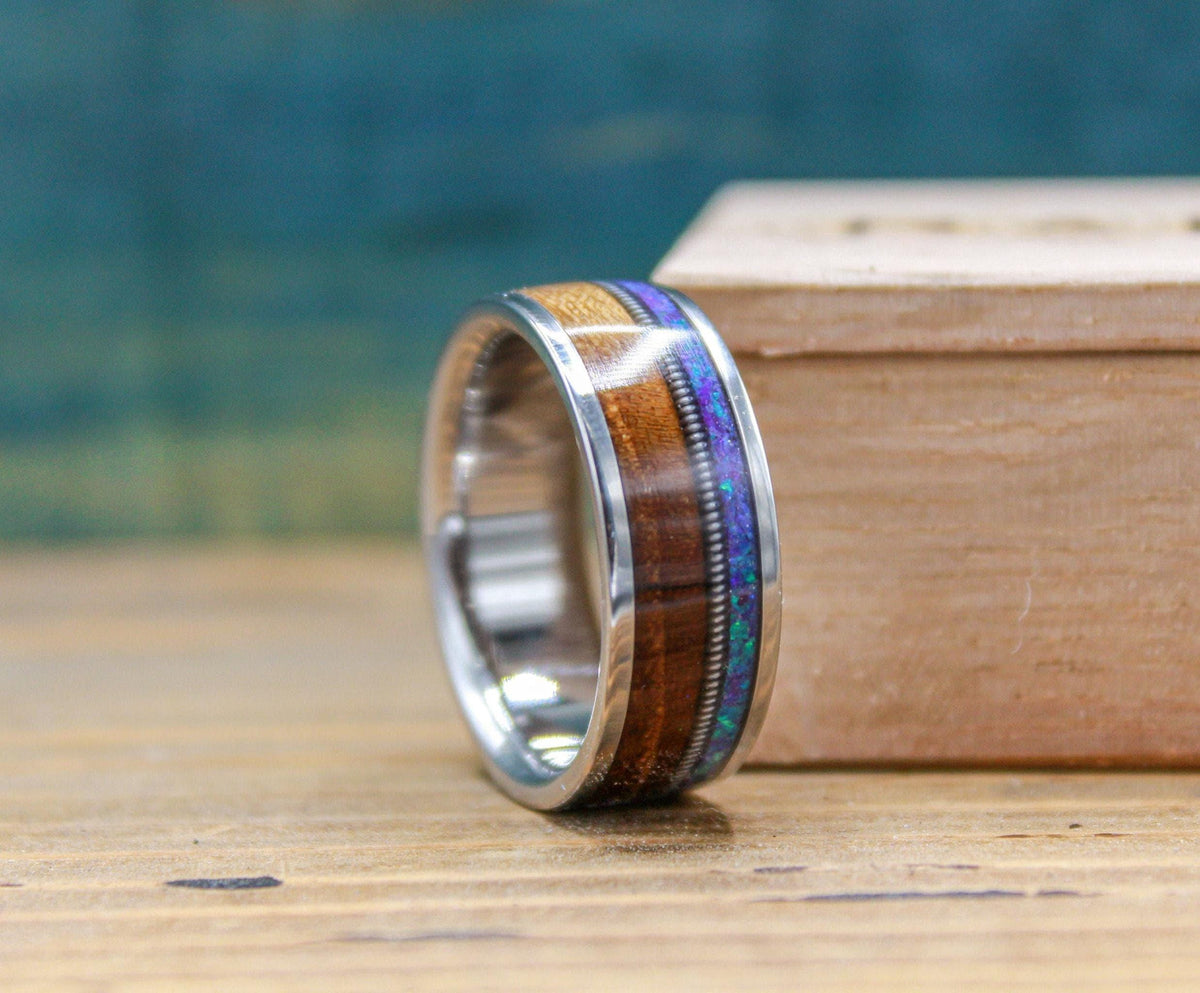 An angled view of a titanium ring featuring a wood, metal, and opal inlay beside a wooden box.