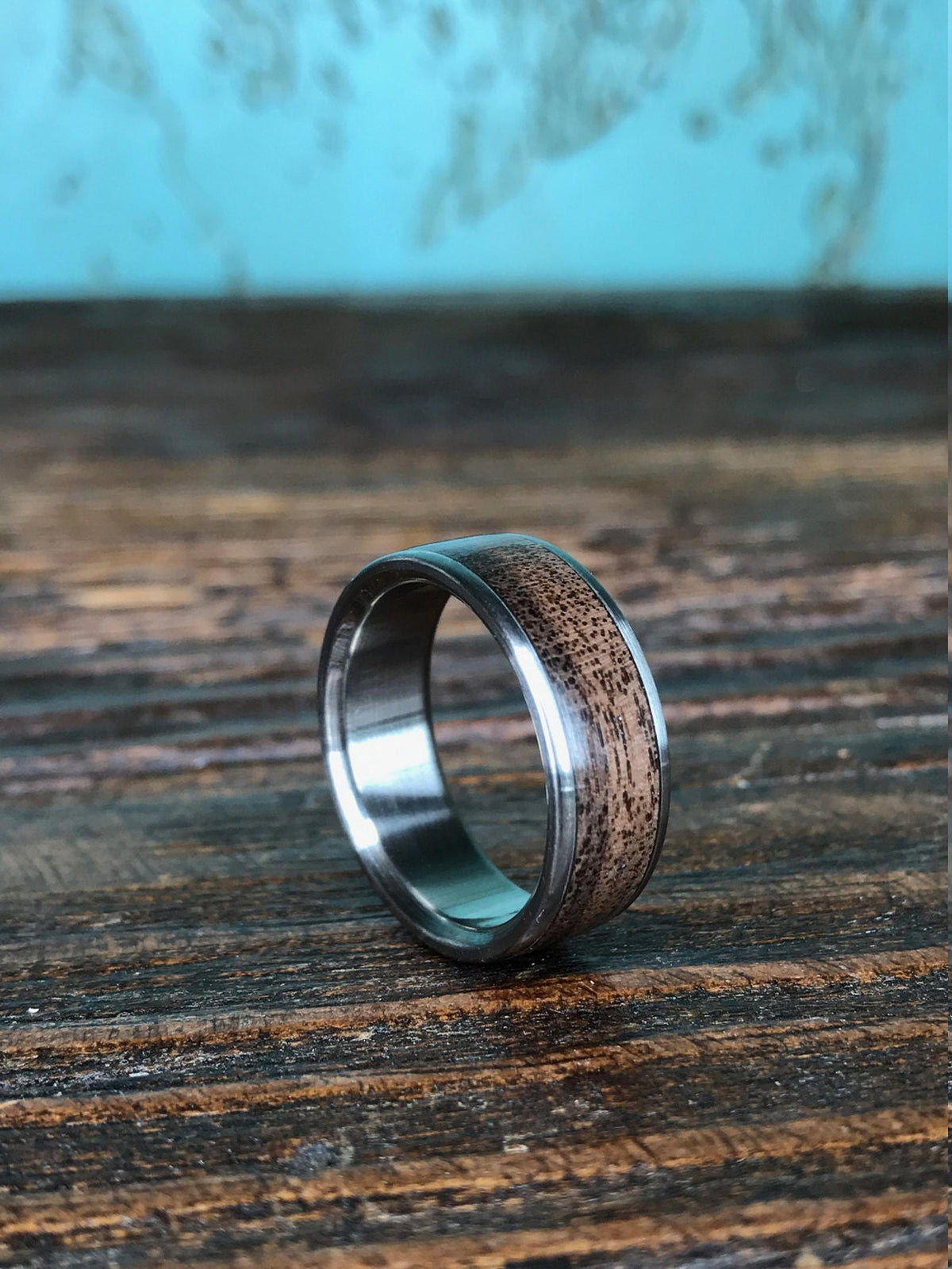 A ring featuring a dark wood inlay and polished silver-colored edges angled upright on a textured wooden surface.