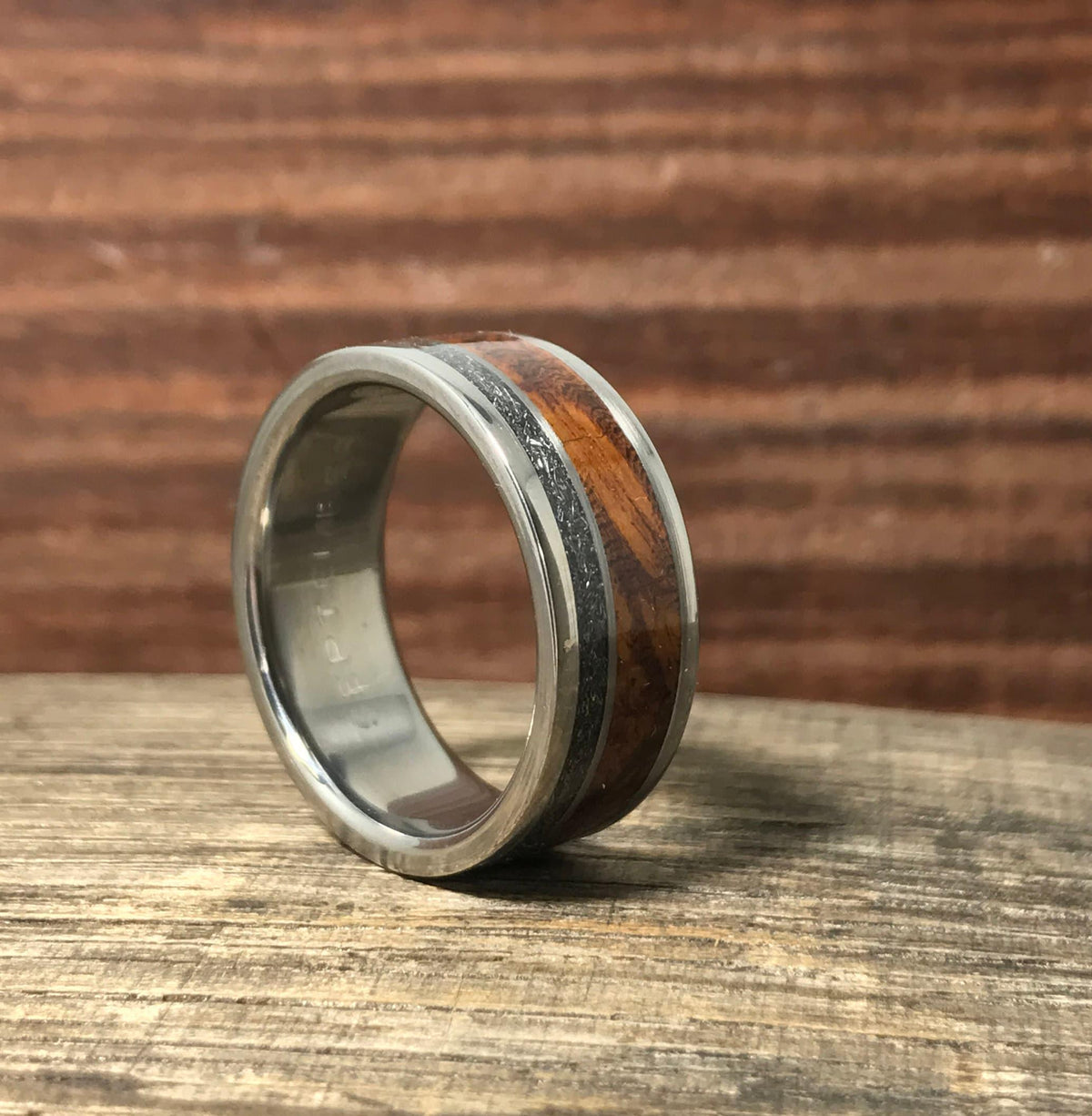 A titanium band with distinctive meteorite and wood inlays angled on a wooden surface.
