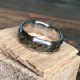 A titanium ring with a black ash burl wood inlay rests on a small piece of light-colored wood.