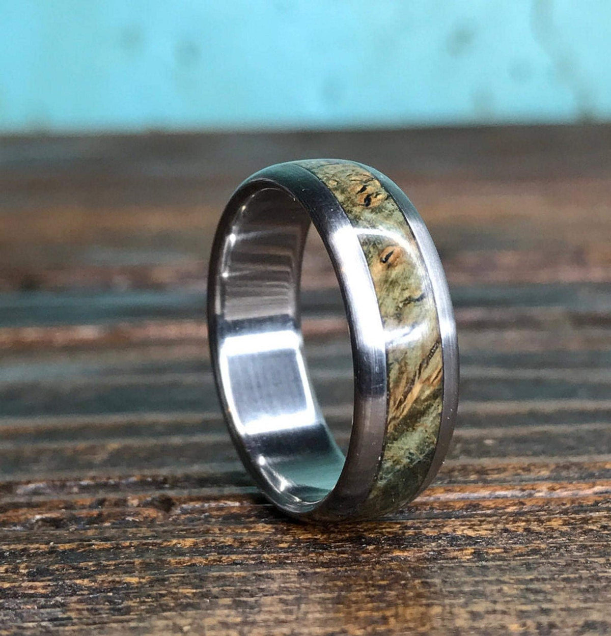 A close-up shot of the titanium and black ash burl ring standing on a dark wooden surface.