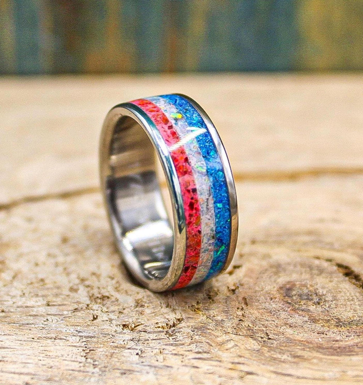 A close-up view of the handmade band angled on a textured wood background, highlighting the polished metal edges surrounding the colorful opal inlay.