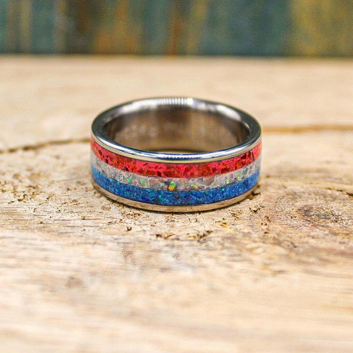 The titanium ring resting flat on the wooden surface, revealing the concentric metal band and horizontal red, white, and blue striped inlay.