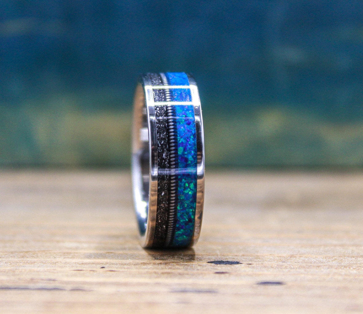 The titanium ring is positioned vertically, highlighting the distinct division between the sparkly blue opal and textured meteorite sections.