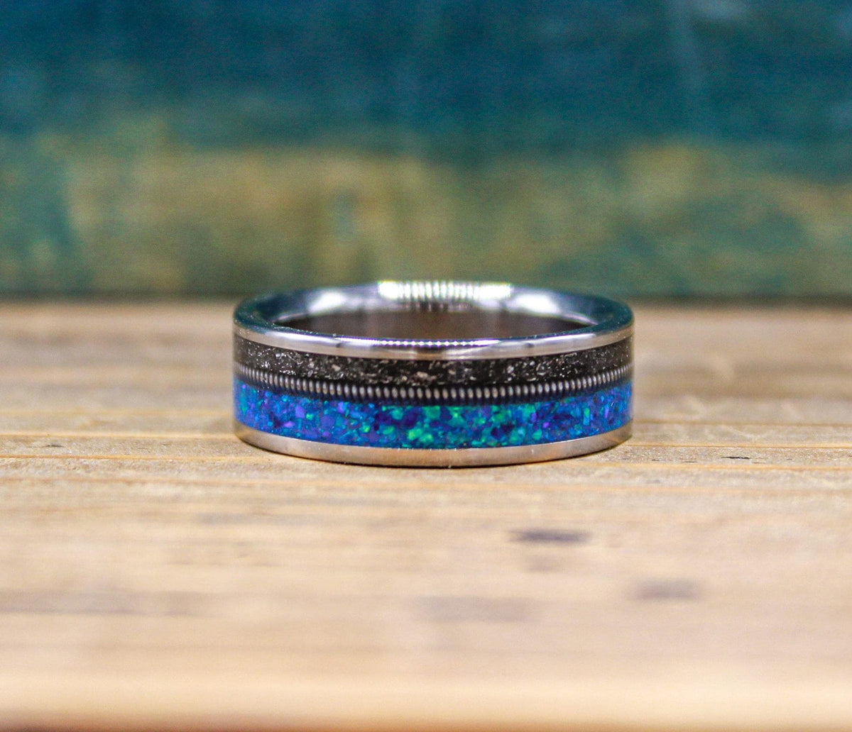 The ring lies flat on a wooden surface, showing its full circumference with the blue opal and meteorite band running along the center.