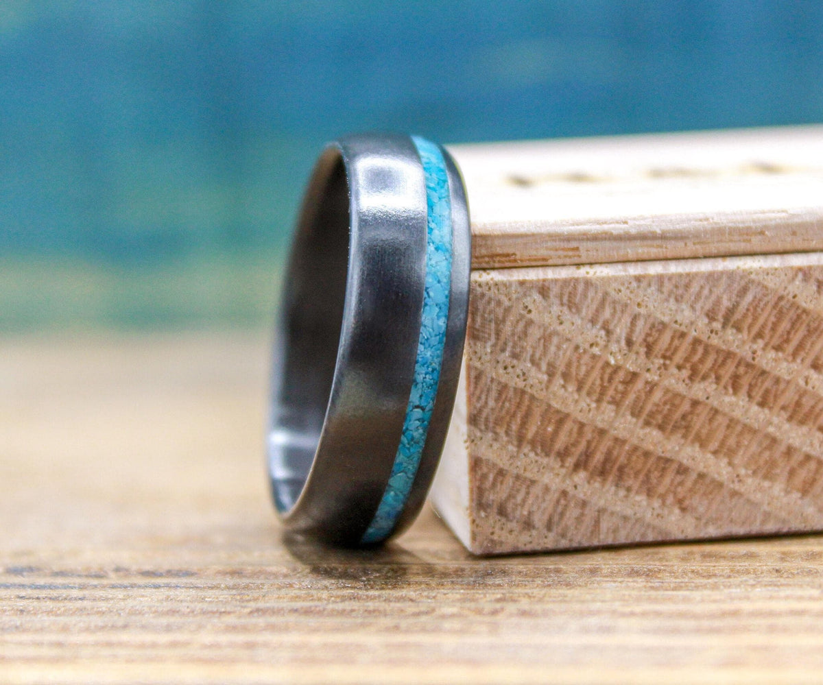 A dark metal ring featuring a central turquoise inlay stands upright next to a wooden box.
