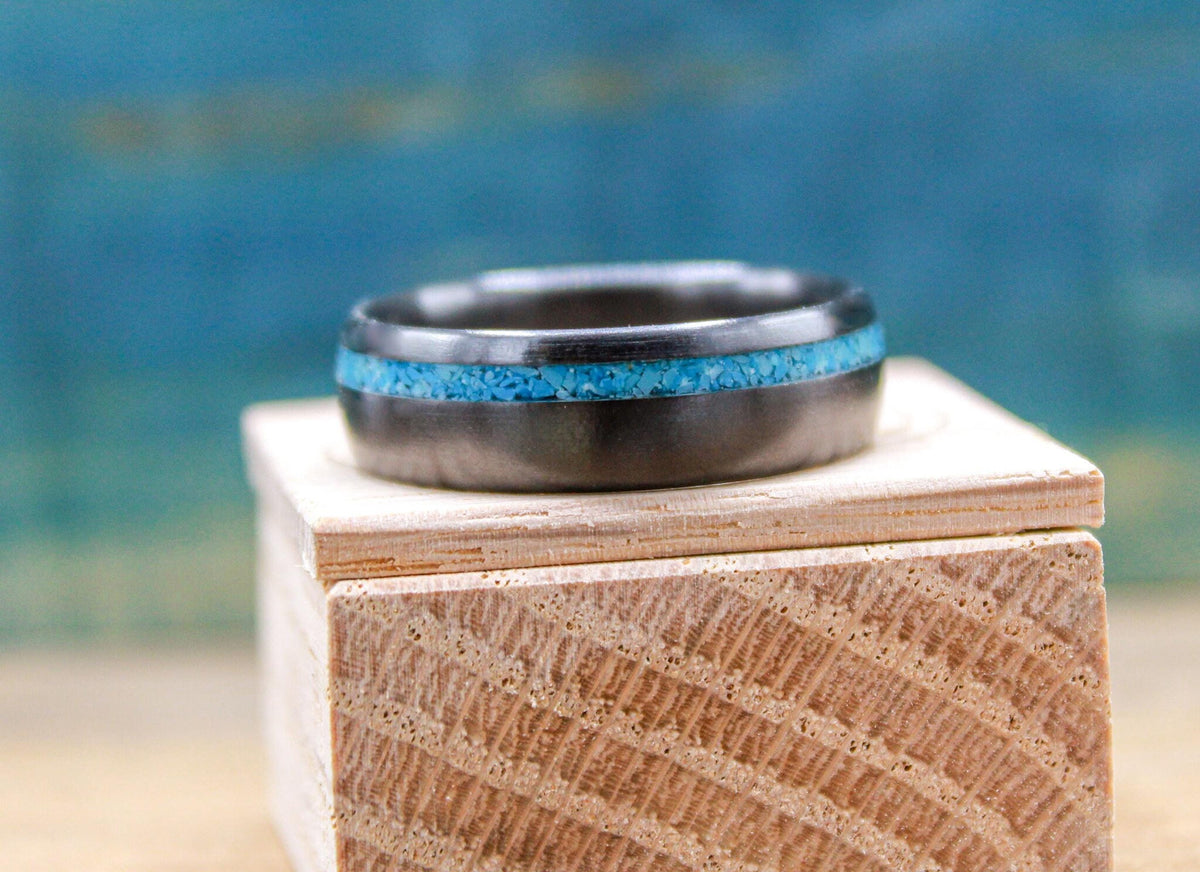 A dark band with a vibrant blue inlay sits flat on top of a small engraved wooden box.