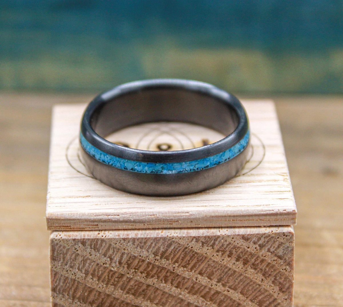 A close-up shot of a dark ring with a vibrant blue inlay resting horizontally on a wooden box.