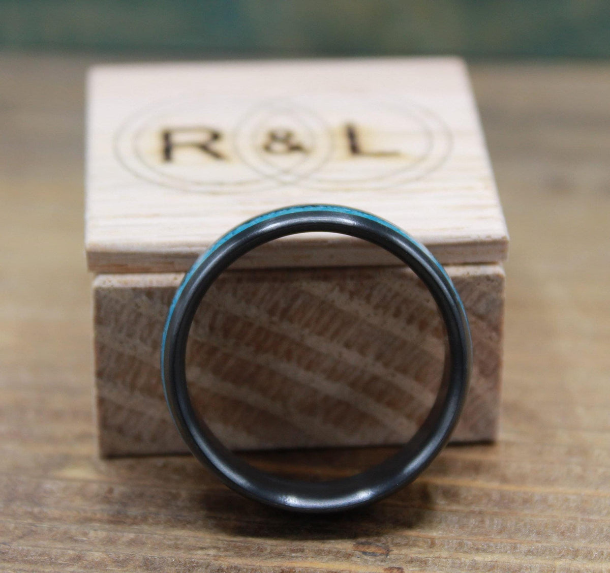 A dark ring stands upright in front of a wooden box stamped with the letters R and L.