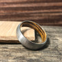 A metal ring with a wood grain interior rests upright on a light wooden block against a rustic wooden background.