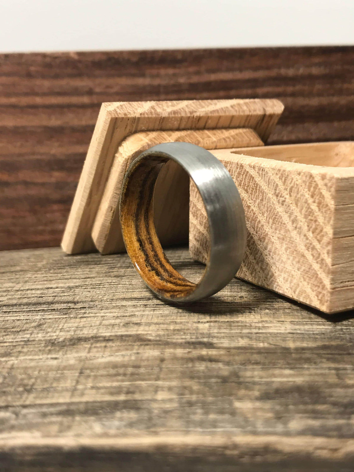A brushed metal ring with a wooden interior stands next to a small open wooden box.