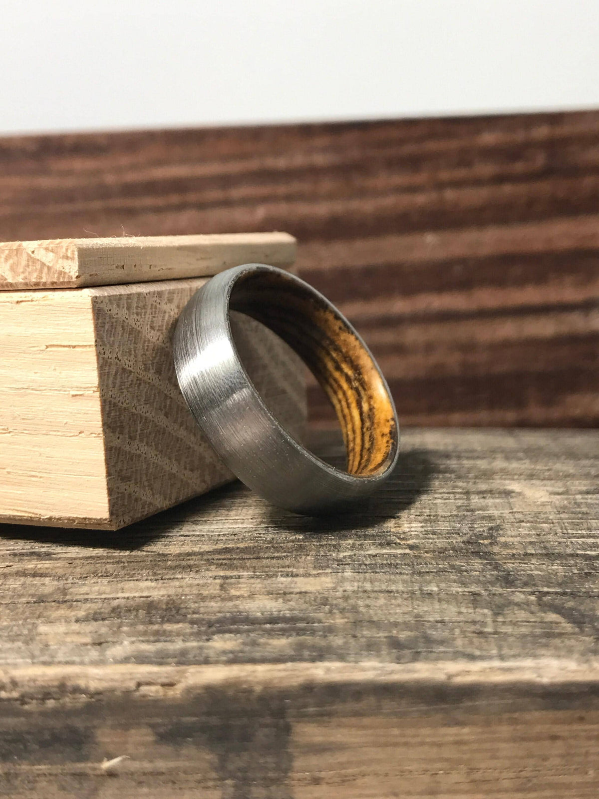 A brushed metal ring with a wooden interior stands upright next to a small wooden box lid on a rustic surface.