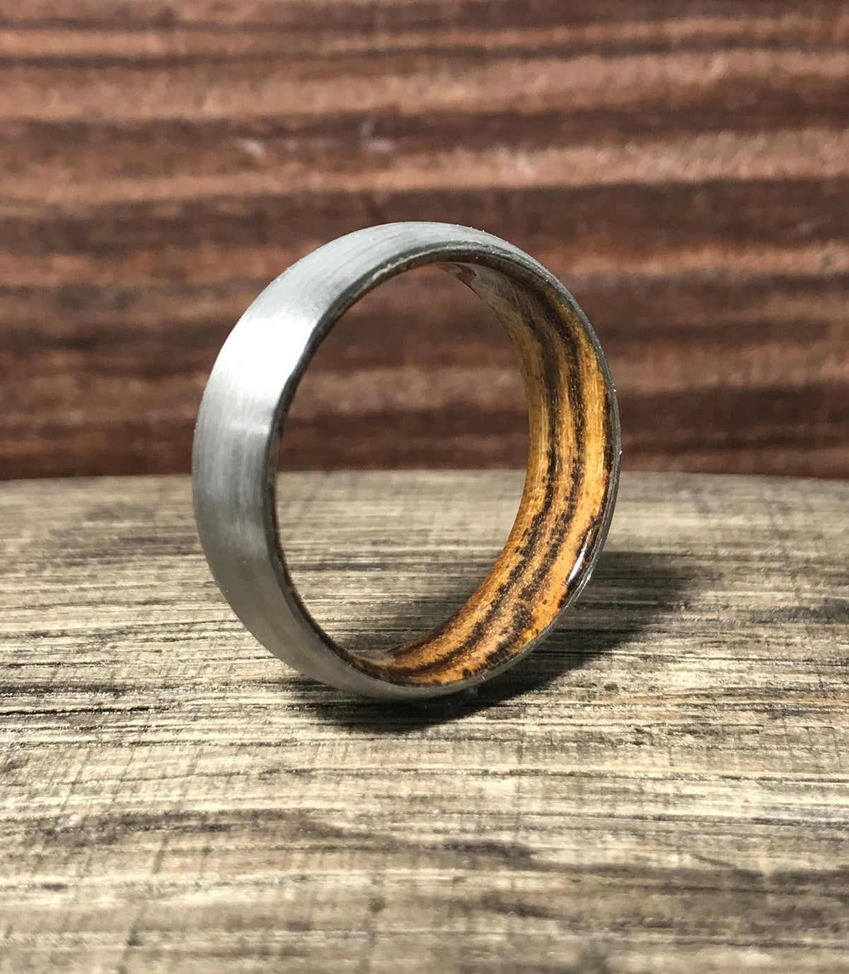 A brushed metal ring with a warm wood interior stands upright on a weathered wooden surface.