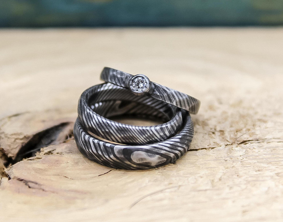 Damascus steel wedding set by RobandLean, featuring his and hers bands with a diamond engagement ring, elegant and handcrafted.