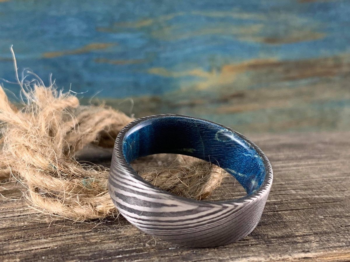 Damascus steel wedding band with blue box elder wood inlay by RobandLean's rings, custom-made wedding ring for special occasions.