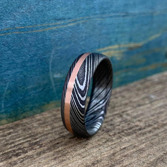 Damascus steel and copper men's wedding band with stainless steel finish, featuring intricate pattern and inlay design.