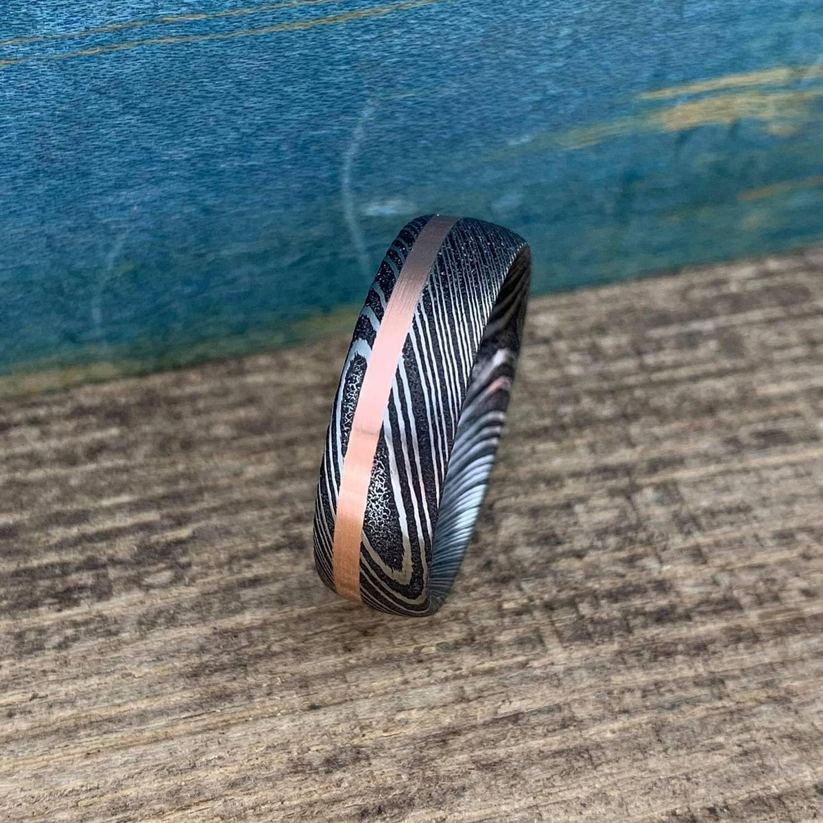 Damascus steel and copper men's wedding band with stainless steel inlay, featuring intricate patterns and a polished finish.