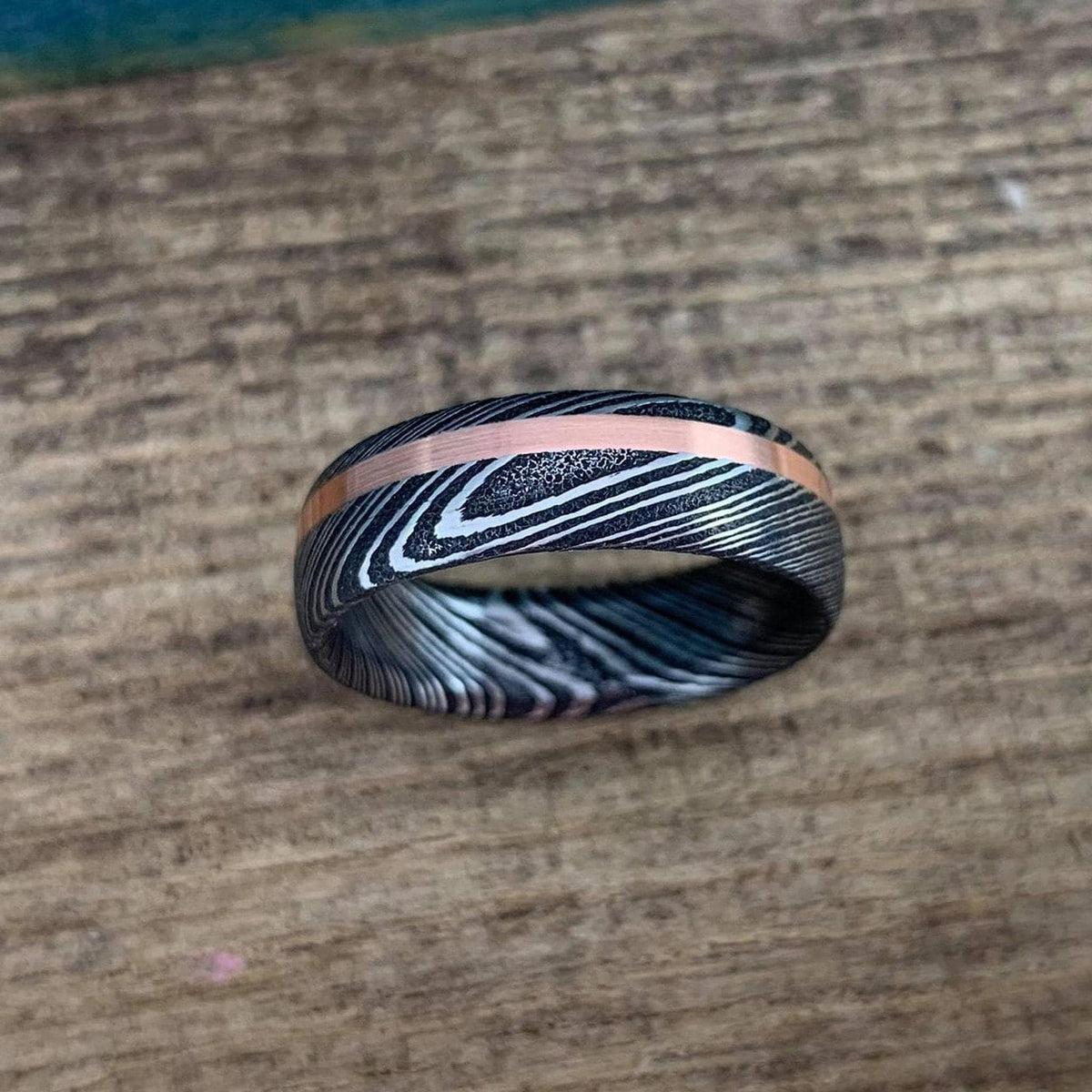 Damascus steel and copper men's wedding band with stainless steel finish, featuring intricate inlay design and polished surface.