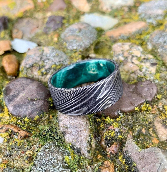 Damascus steel wedding band with green wood inlay by RobandLean's rings, showing the detailed textured metal and vibrant inlay design.