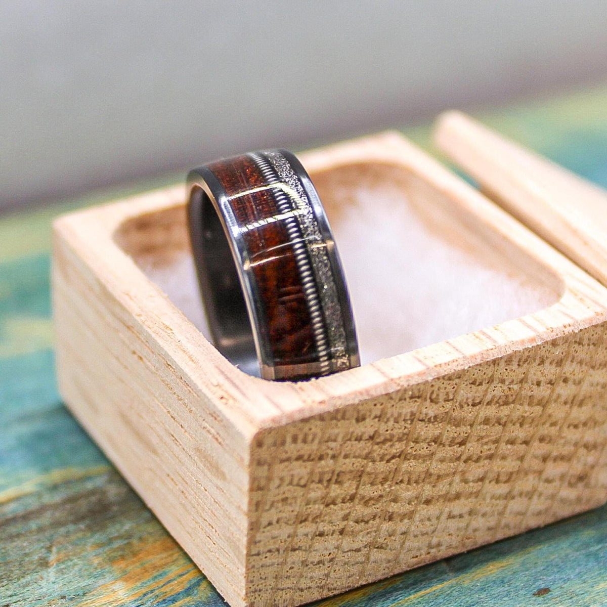 Black titanium men's wedding band with rosewood inlay, meteorite accent, and embedded guitar string, crafted by RobandLean's rings.