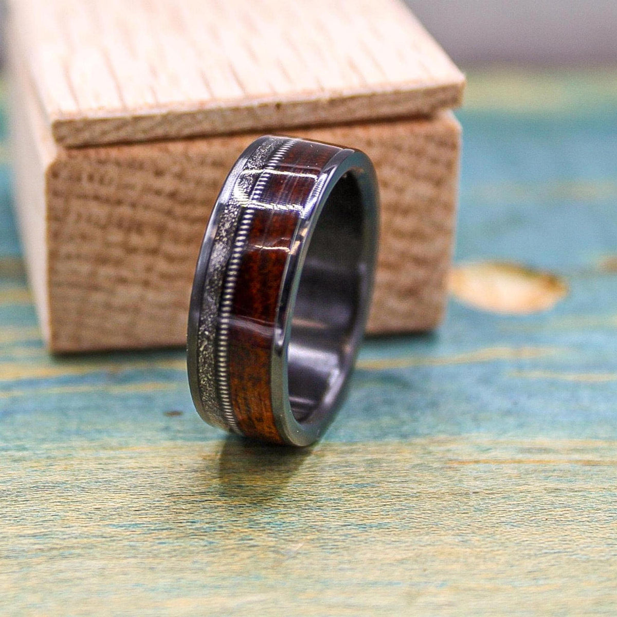 Black titanium wedding band with rosewood inlay, meteorite accents, and guitar string detail, designed for men's wedding jewelry.