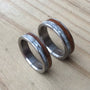 A pair of titanium rings with mother of pearl and ancient kauri wood inlays, placed on a wooden surface.