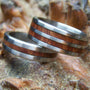 A pair of titanium rings with manzanita burl wood inlay, placed on a natural wooden surface.
