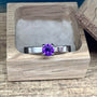 A titanium and amethyst solitaire ring is displayed in a handmade oak ring box, with the ring's purple gemstone clearly visible.