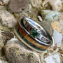 A titanium ring with a segment of English oak wood and a piece of moss agate, alongside a shed deer antler, placed on a rock. alongside a moss agate prong set ring