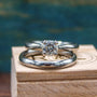 A titanium wedding ring set featuring a plain rounded band and a prong set band with a clear moissanite center stone, displayed on a wooden block with a blurred blue background.