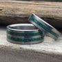 A set of two titanium rings, both with a green malachite stone inlay, placed on a wooden surface.