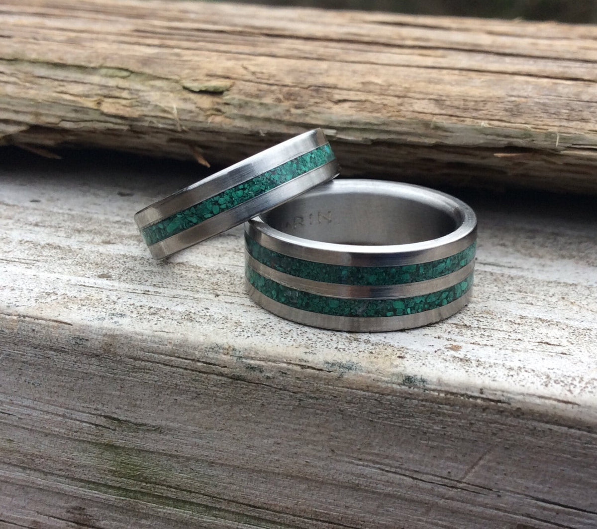 His and hers titanium couples rings with malachite in a matching wedding band set, featuring sleek silver-colored bands and green gemstone accents.