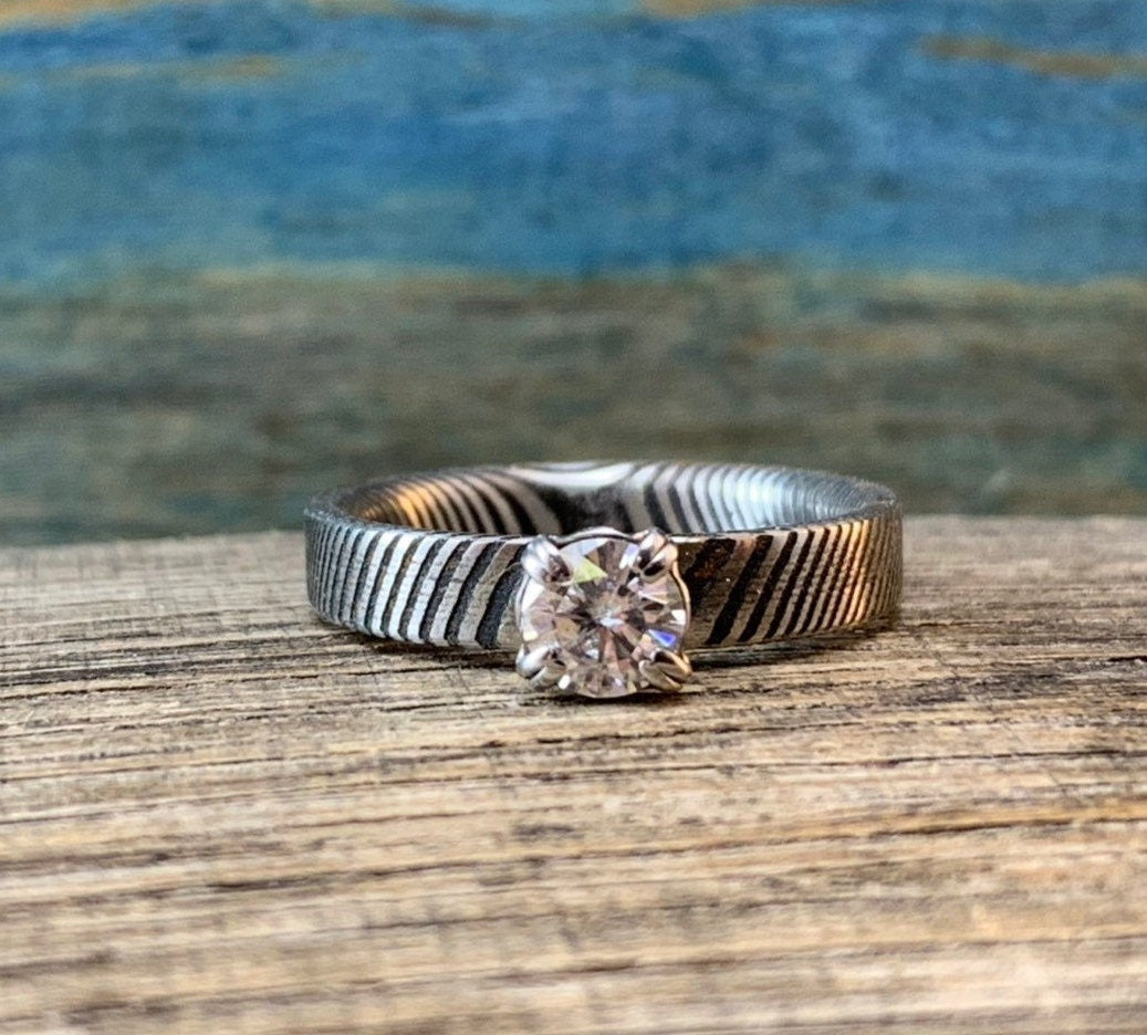 Ladies Moissanite Damascus Steel Engagement Ring with intricate pattern and sparkling gemstone, crafted by RobandLean's rings.