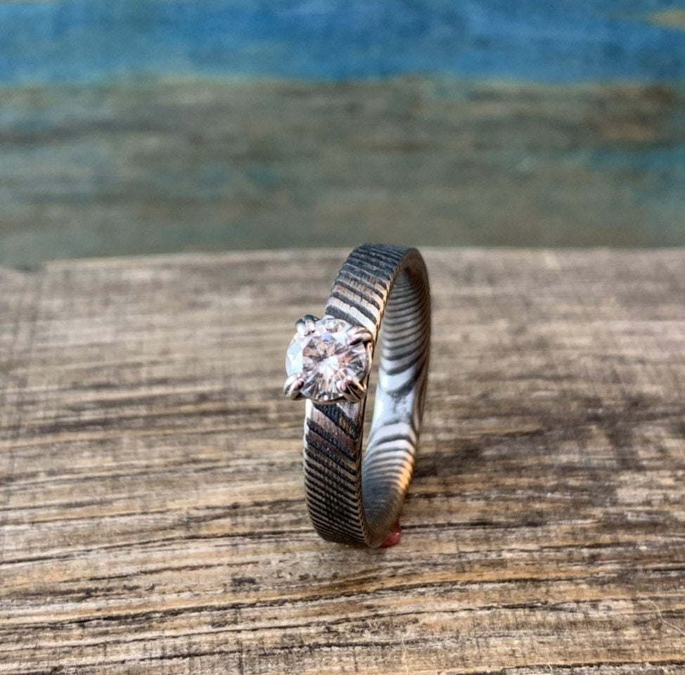 Ladies moissanite Damascus steel engagement ring showcasing a sleek band with sparkling moissanite stones and intricate Damascus pattern.